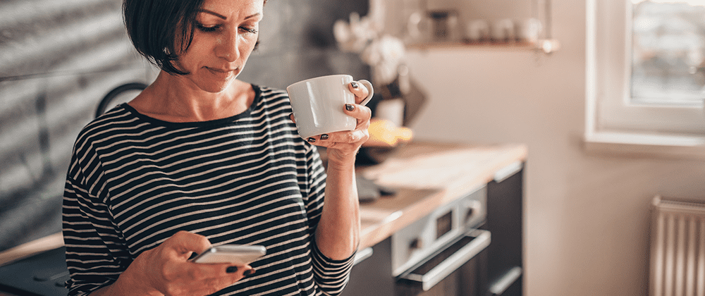 woman holding coffee in left hand while looking down at phone in right hand